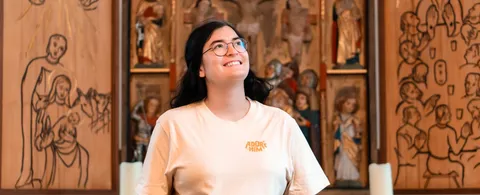 Person im hellen „Adore Him“-Shirt vor einem geschnitzten Altar